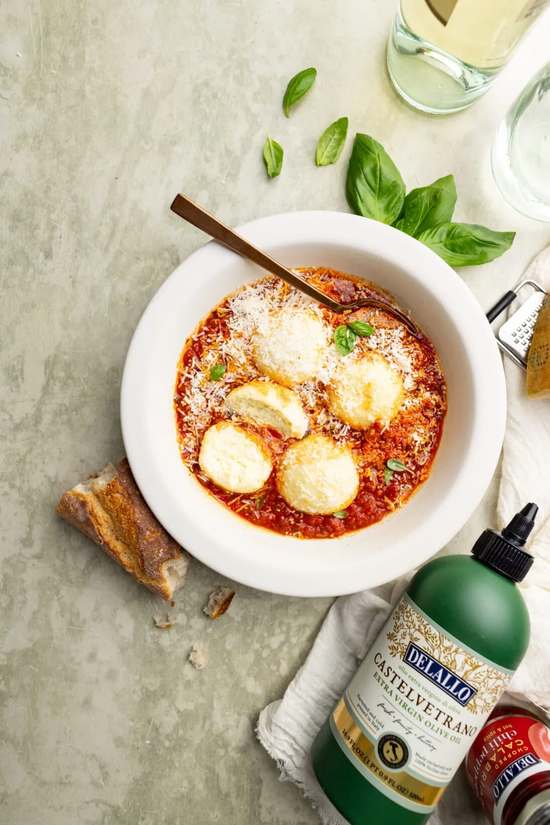 a bowl of ricotta gnudi in a spicy red sauce topped with Parmesan cheese next to Delallo products.