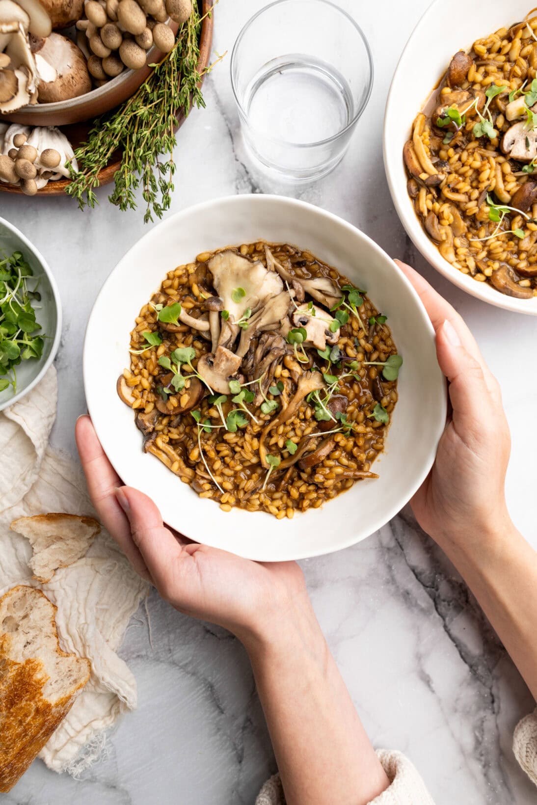holding a bowl of mushroom barley risotto topped with micro greens