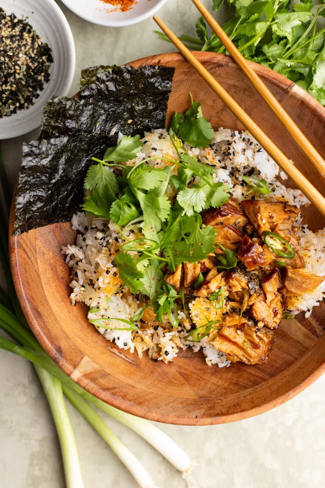 crispy rice bowl topped with salmon, green onions, cilantro, and nori sheets.