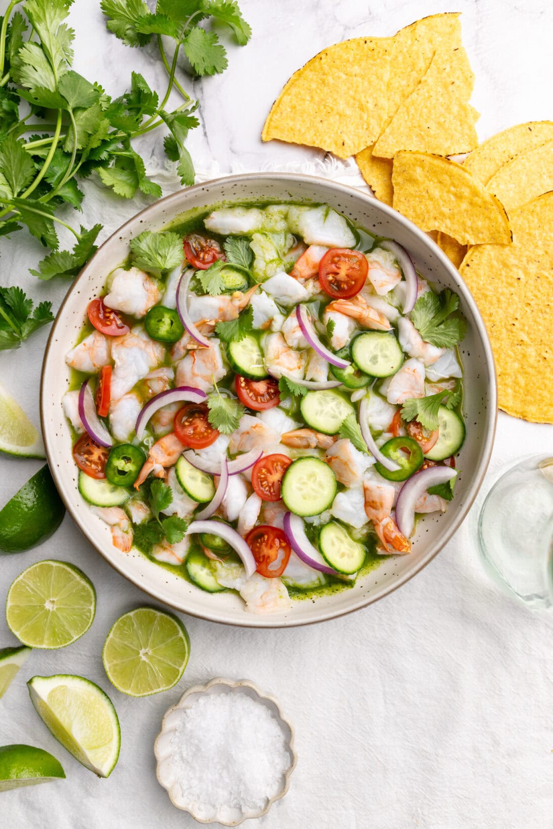 Aguachile in a bowl topped  with cucumbers, tomatoes, red onion.