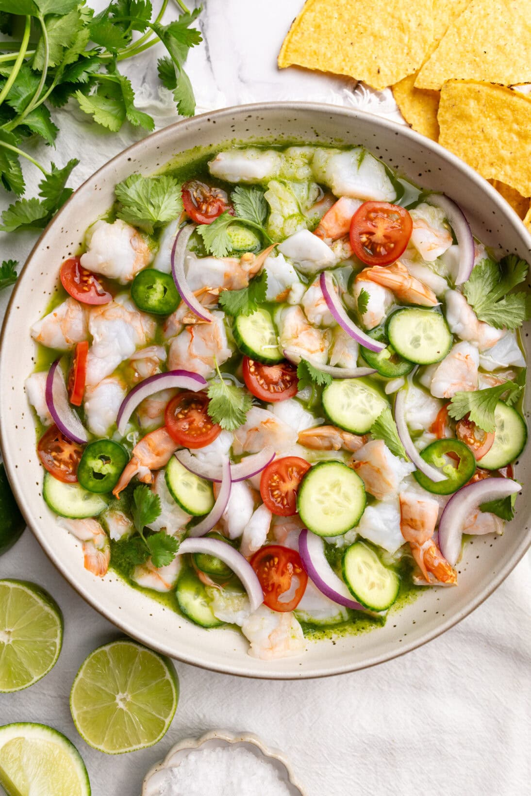 Aguachile in a bowl topped  with cucumbers, tomatoes, red onion.