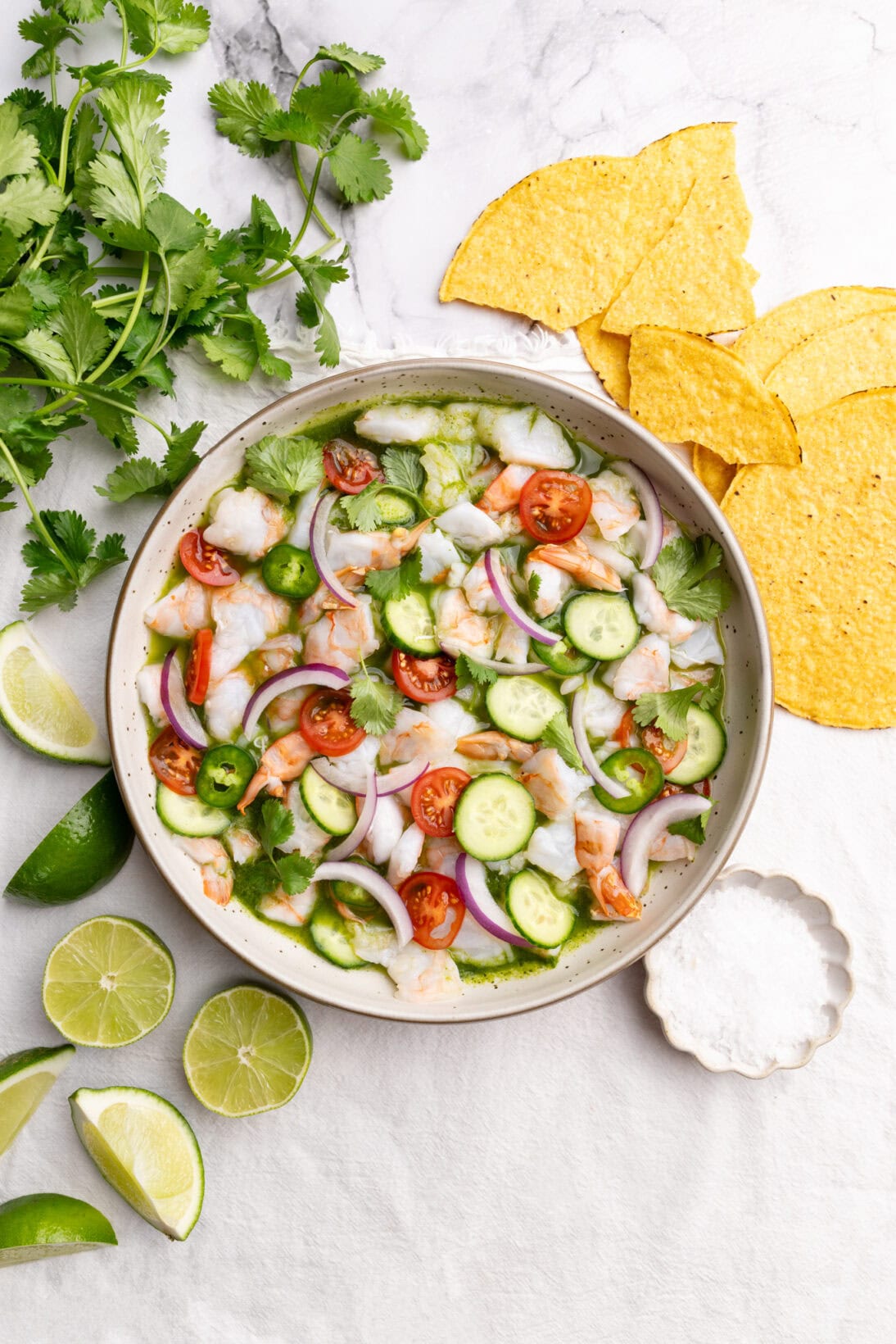 Aguachile in a bowl topped  with cucumbers, tomatoes, red onion. 