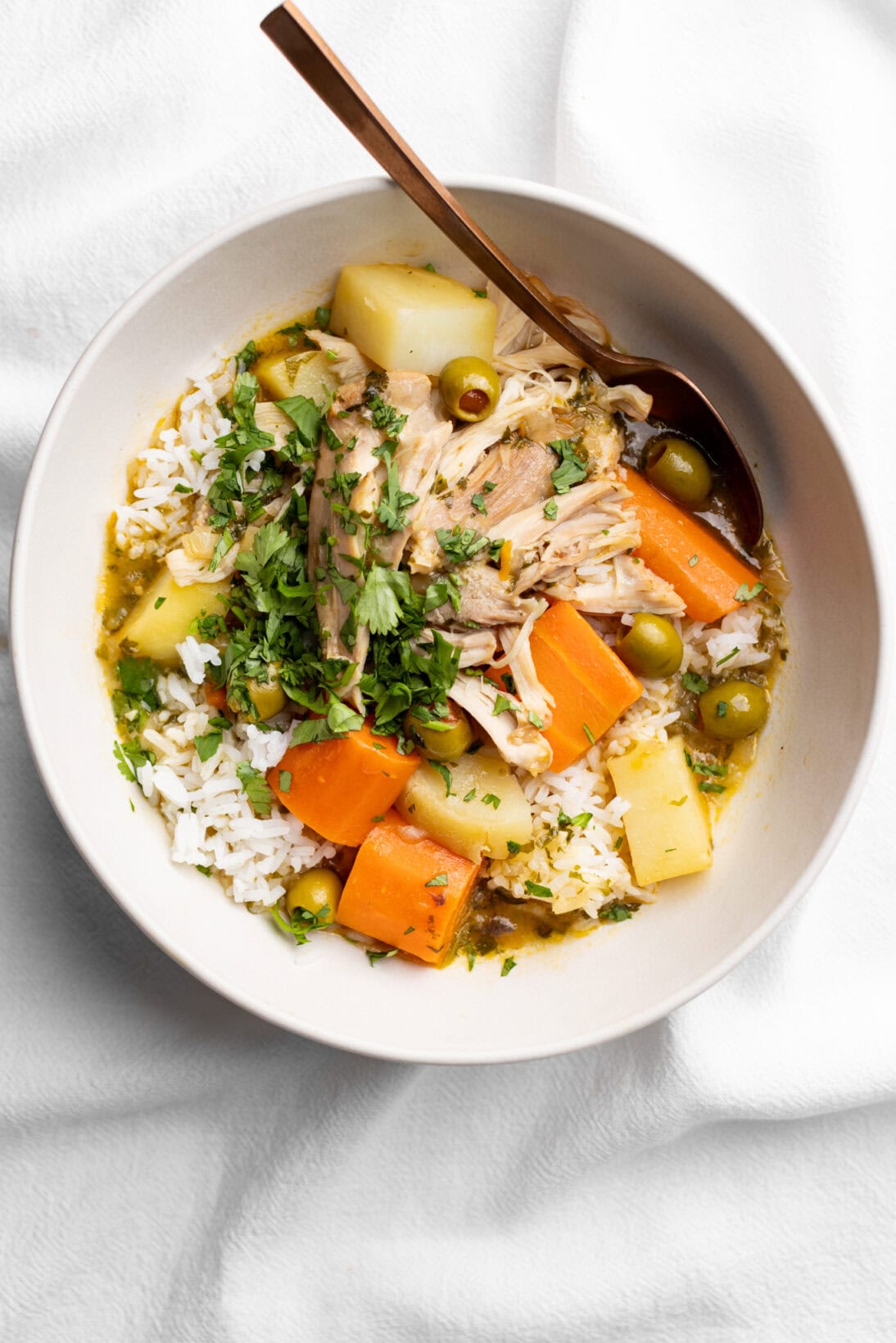 A bowl of pollo guisado, fall off the bone chicken thighs, chunky carrots, potatoes, green olives over rice.