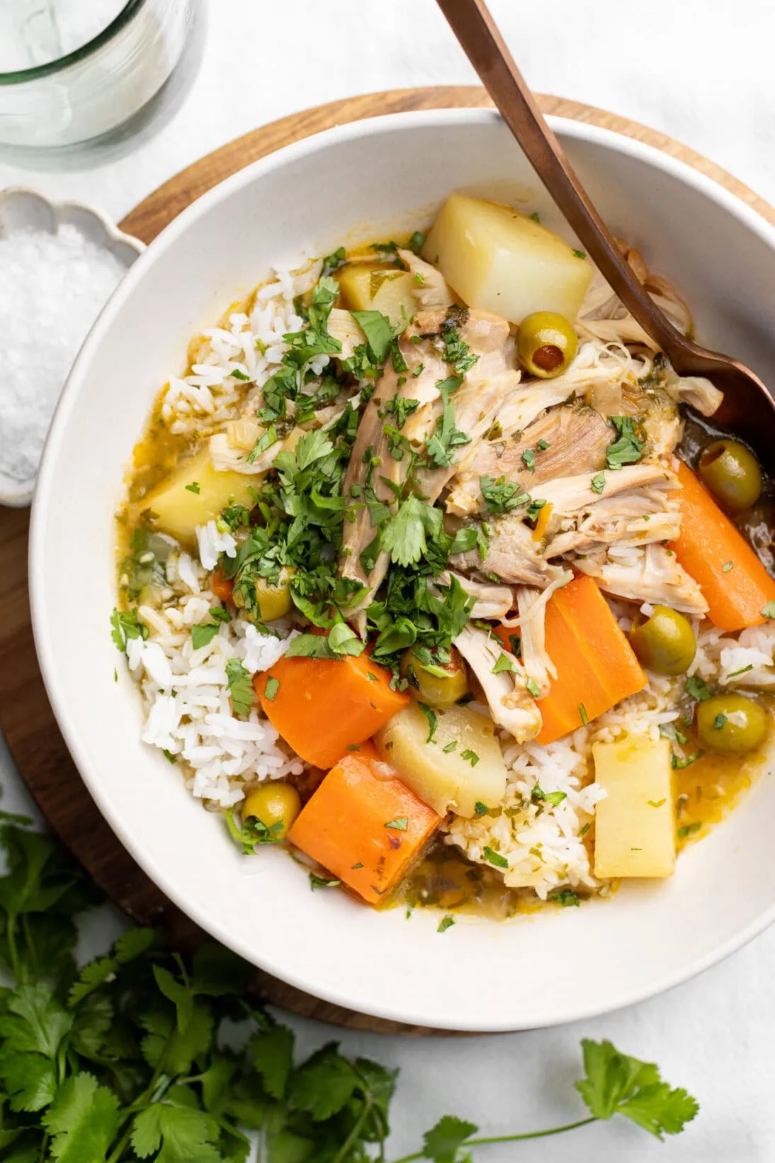 A bowl of pollo guisado, fall off the bone chicken thighs, chunky carrots, potatoes, green olives over rice.