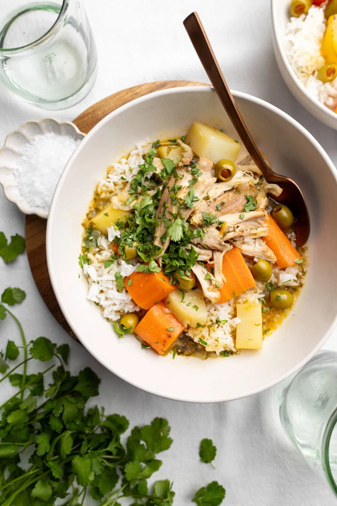 A bowl of pollo guisado, fall off the bone chicken thighs, chunky carrots, potatoes, green olives over rice.