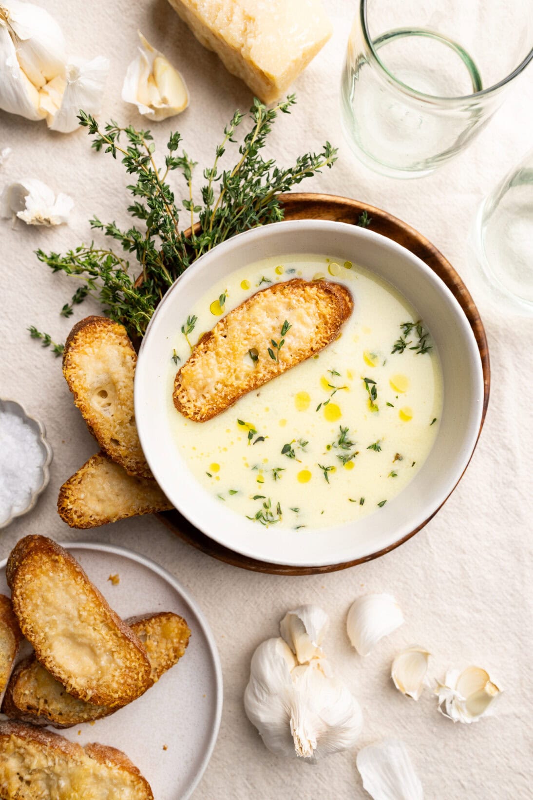 A bowl of country French garlic soup, topped with fresh thyme and a cheesy crostini.