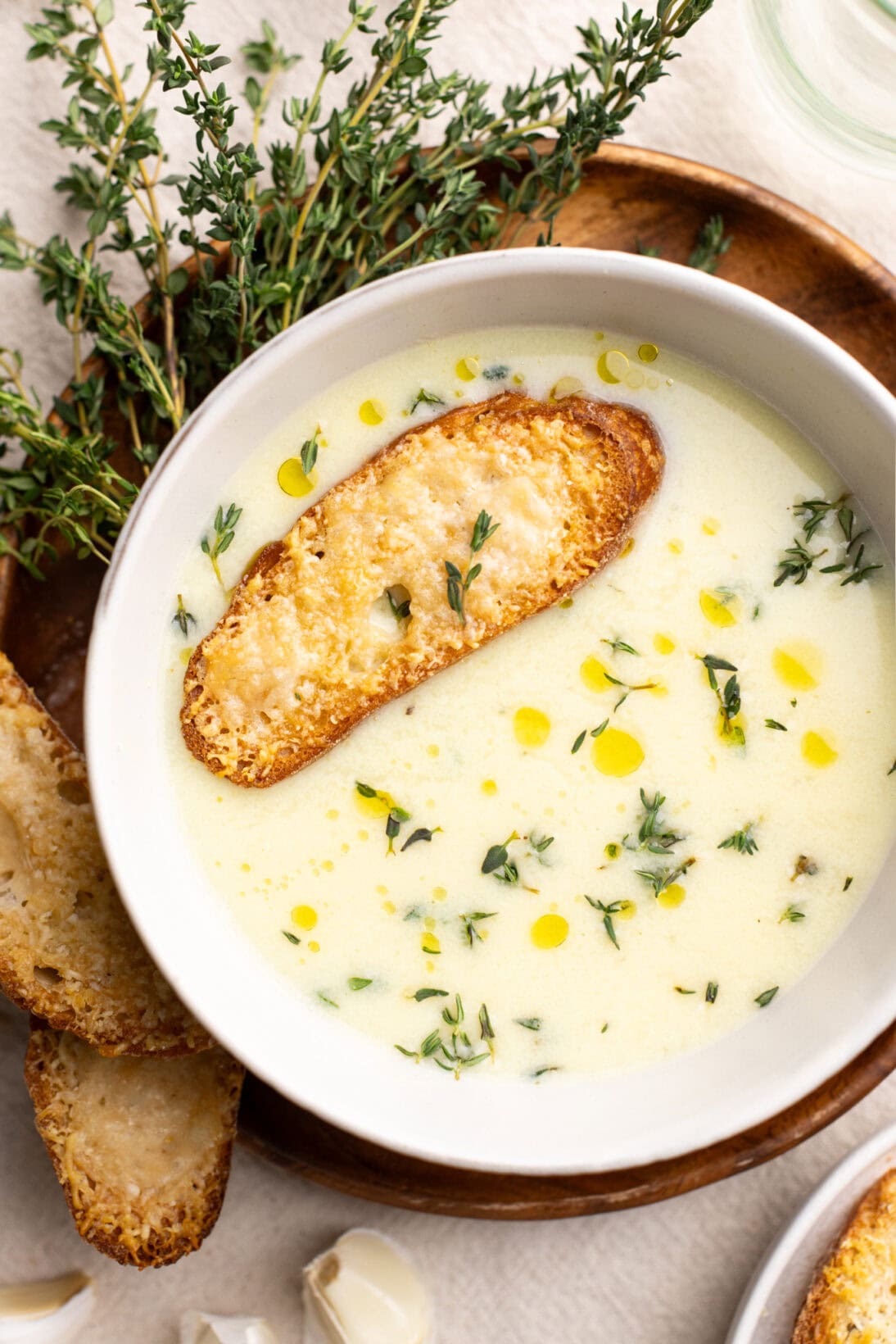 A bowl of country French garlic soup, topped with fresh thyme and a cheesy crostini.