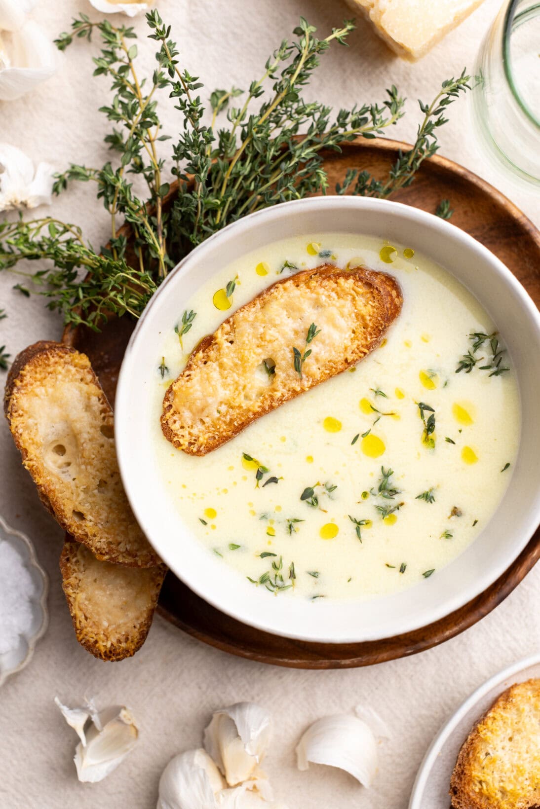 A bowl of country French garlic soup, topped with fresh thyme and a cheesy crostini.