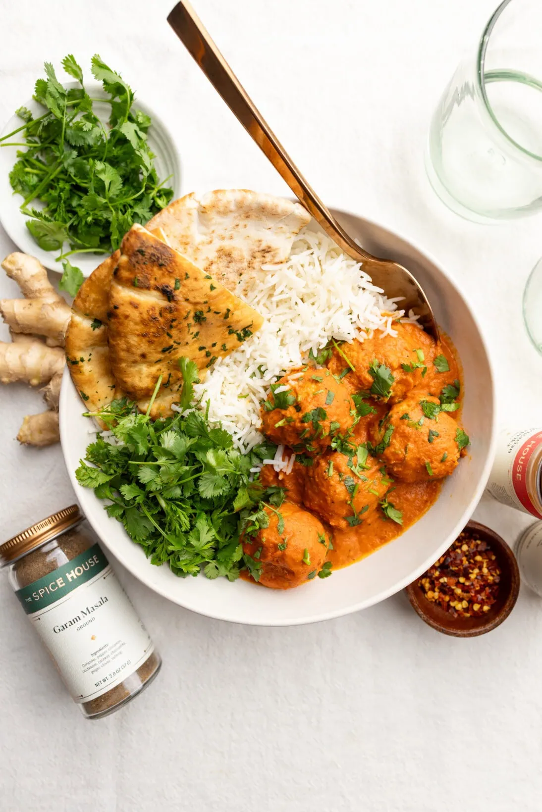 bowl of butter chicken meatballs served with basmati rice, pita bread, and extra cilantro