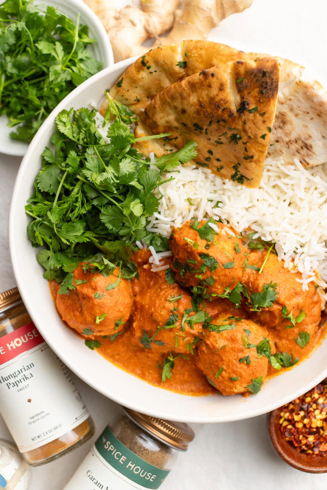 up close bowl of butter chicken meatballs served with basmati rice, pita bread, and extra cilantro