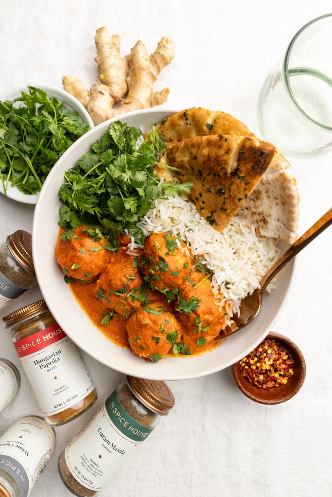 bowl of butter chicken meatballs served with basmati rice, pita bread, and extra cilantro