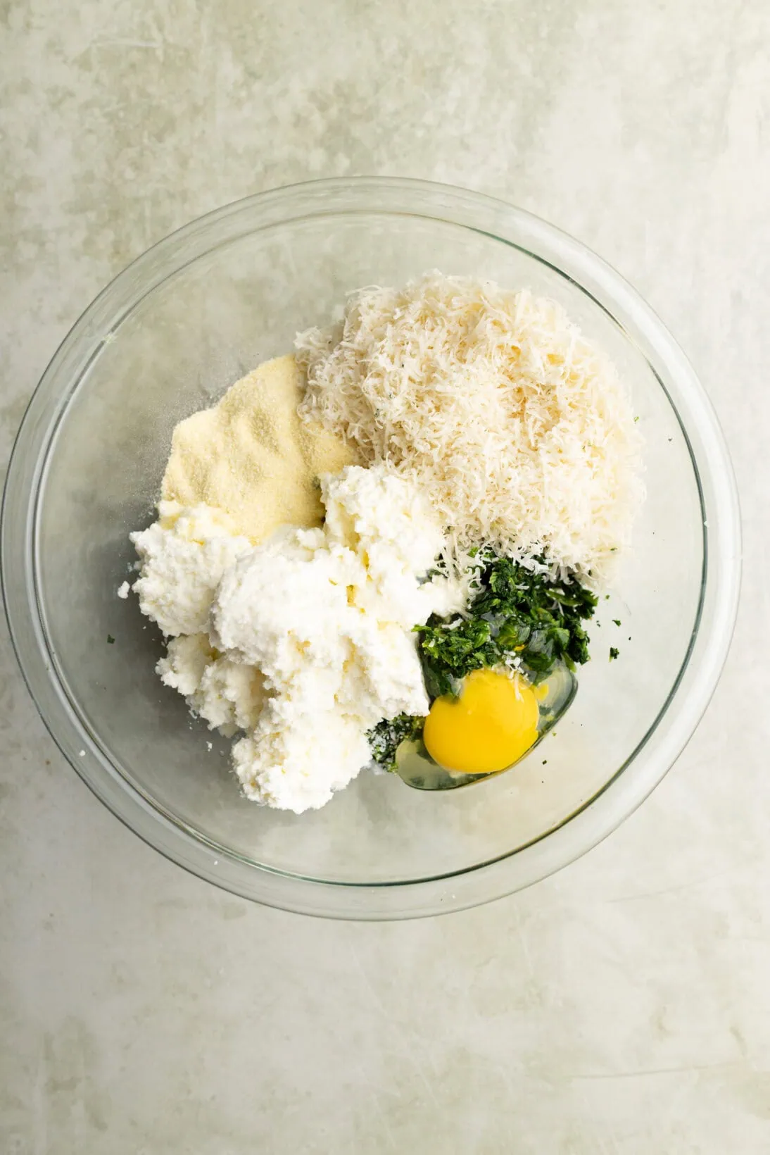 ingredients portioned in a bowl (ricotta, semolina, parm, spinach, and egg)