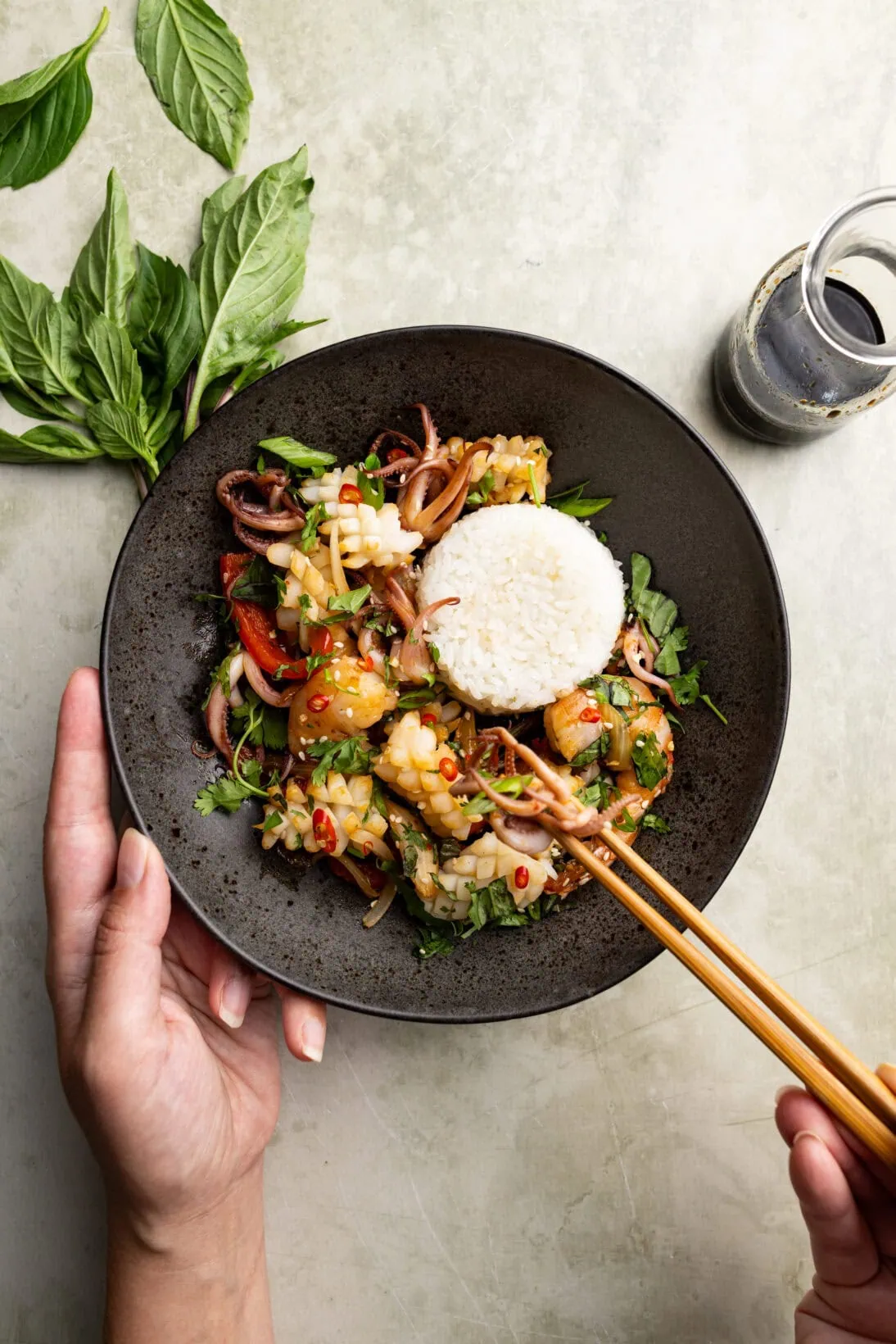 pulling a piece of squid from a bowl of Thai spicy squid stir fry served with sushi rice.