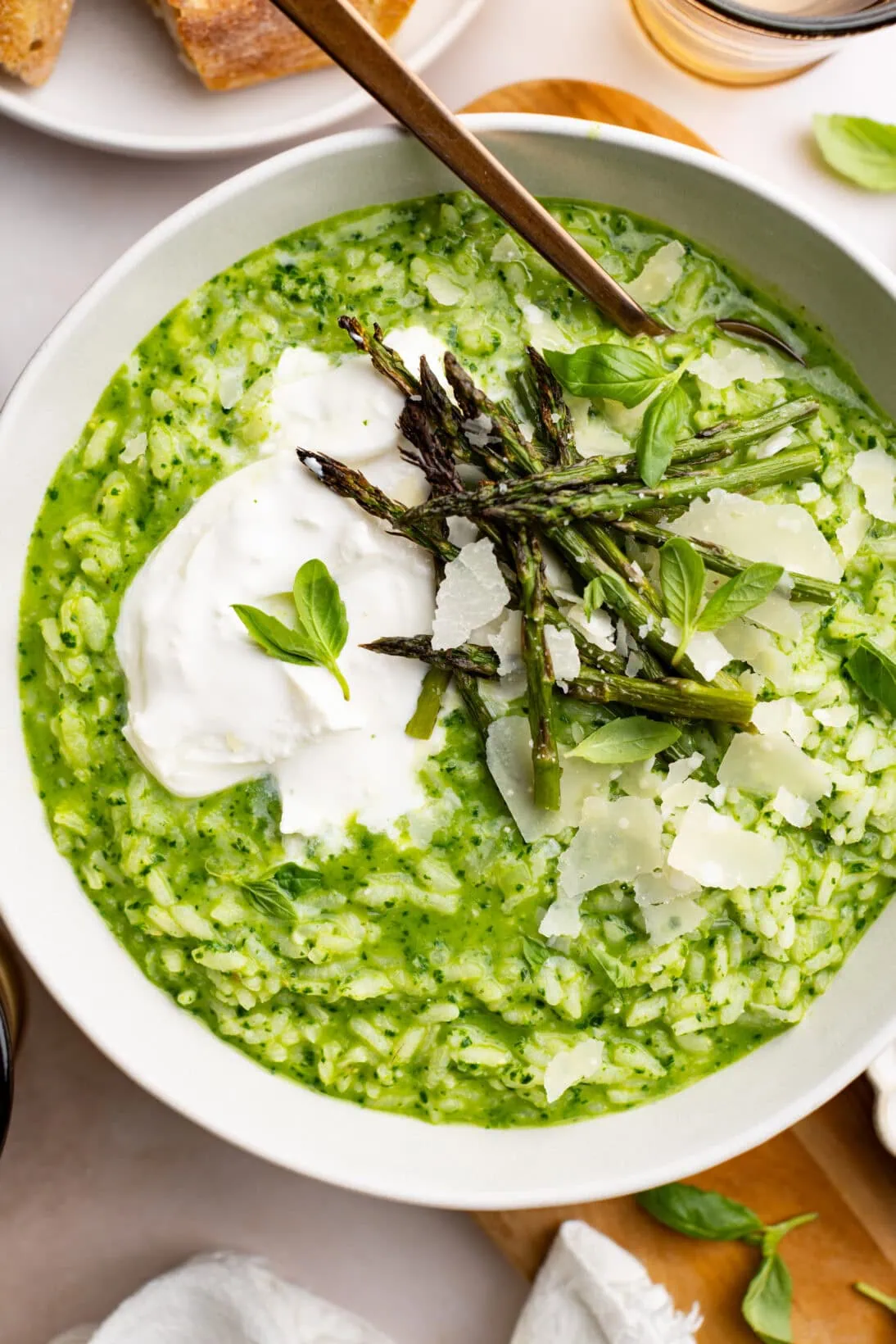 up close bowl of pesto risotto topped with burrata, roasted asparagus and shaved Parmesan cheese.