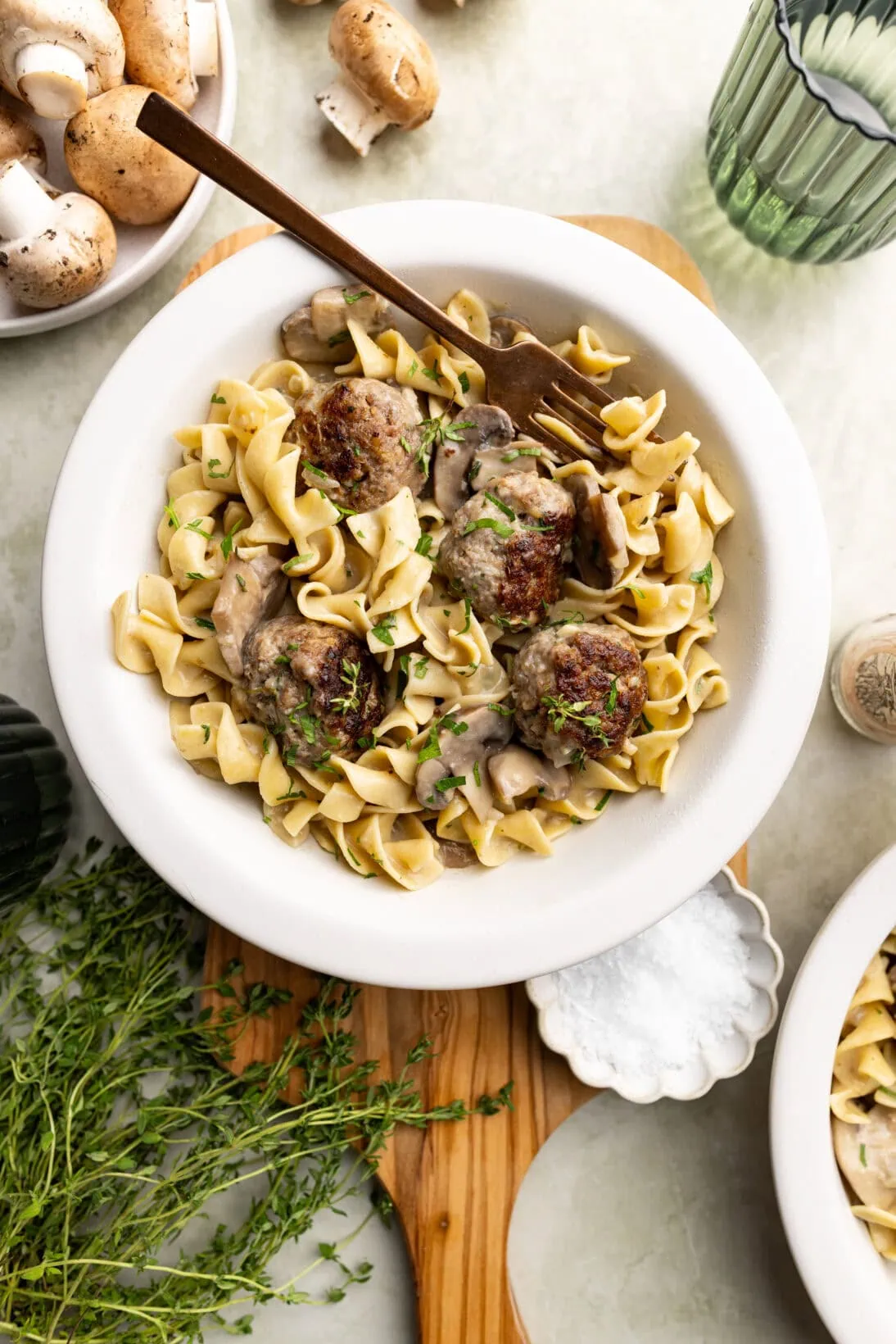 a bowl of beef stroganoff meatballs on a wooden board topped with parsley and thyme.