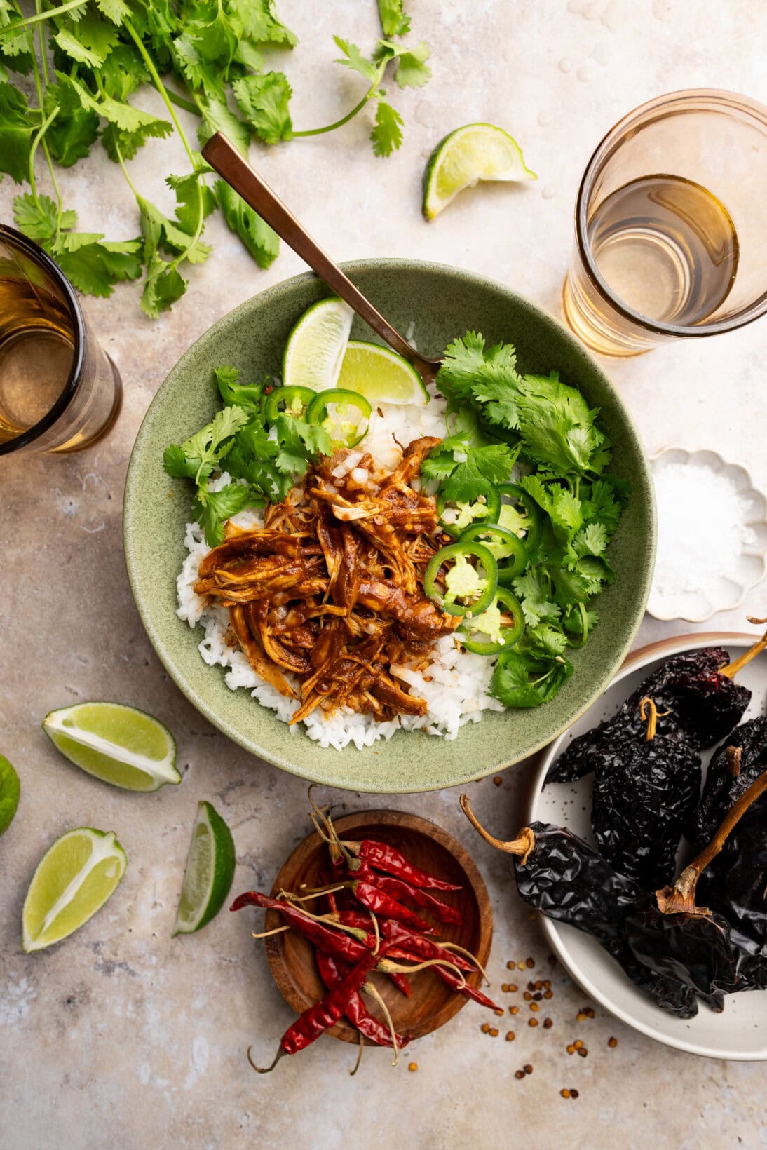 Chicken birria in a bowl over white rice topped with cilantro, white onions, jalapeños and wedges of lime.