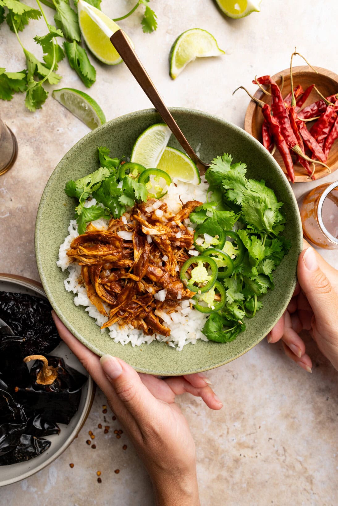 Chicken birria in a bowl over white rice topped with cilantro, white onions, jalapeños and wedges of lime.