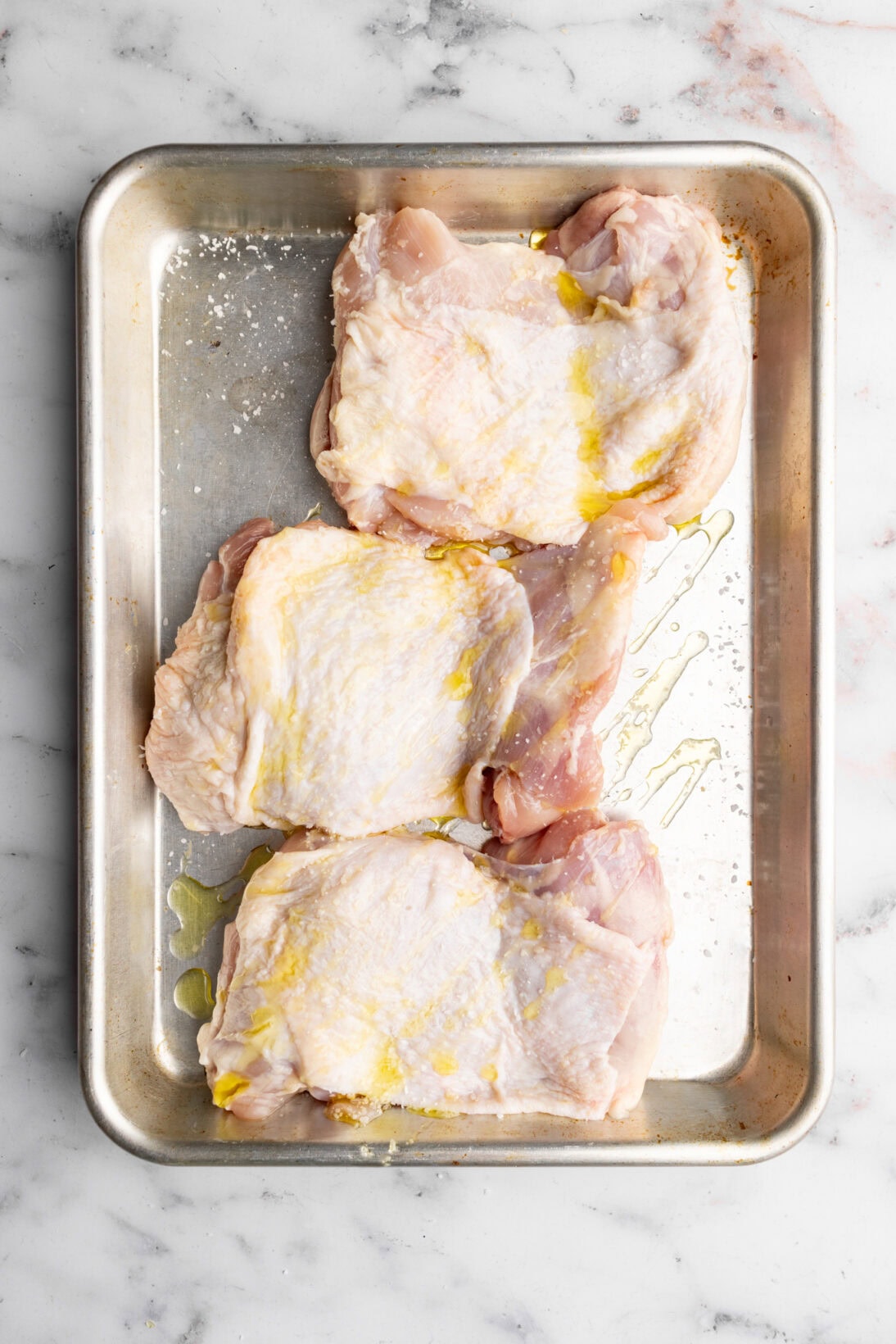 step by step: chicken thighs on a sheet pan seasoned with olive oil and kosher salt.