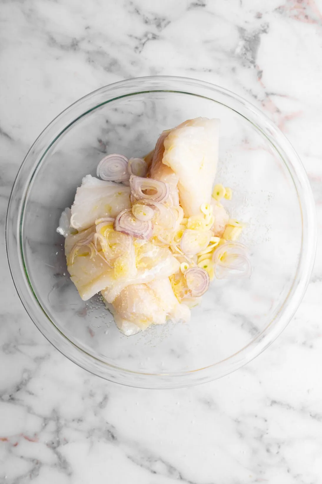 step by step: bowl of butchered cod with shallots, sliced garlic cloves, extra- virgin olive oil and salt.