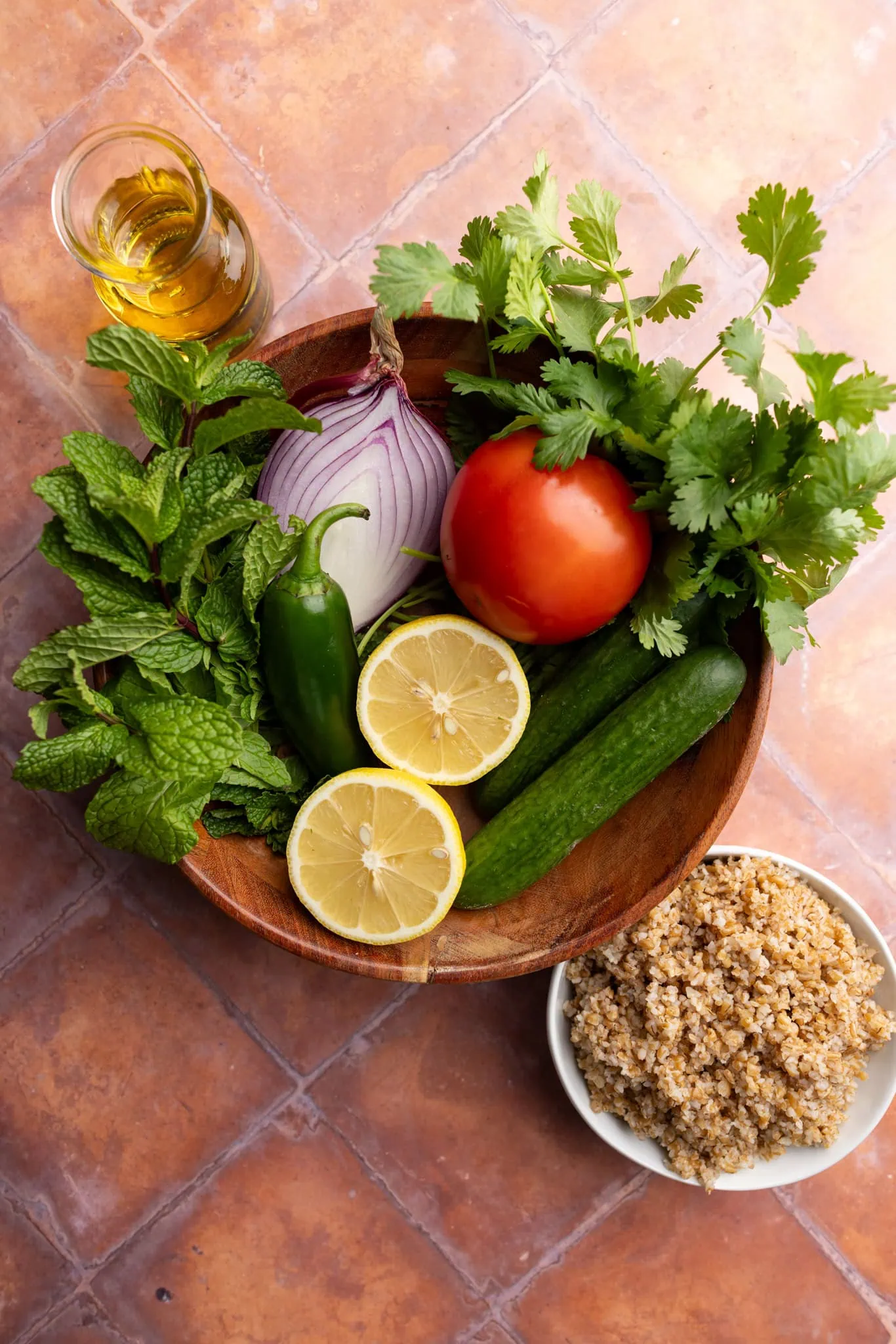ingredients in a bowl: cucumber, tomato, lemon, jalapeno, red onion, mint, cilantro, bulgur, olive oil.