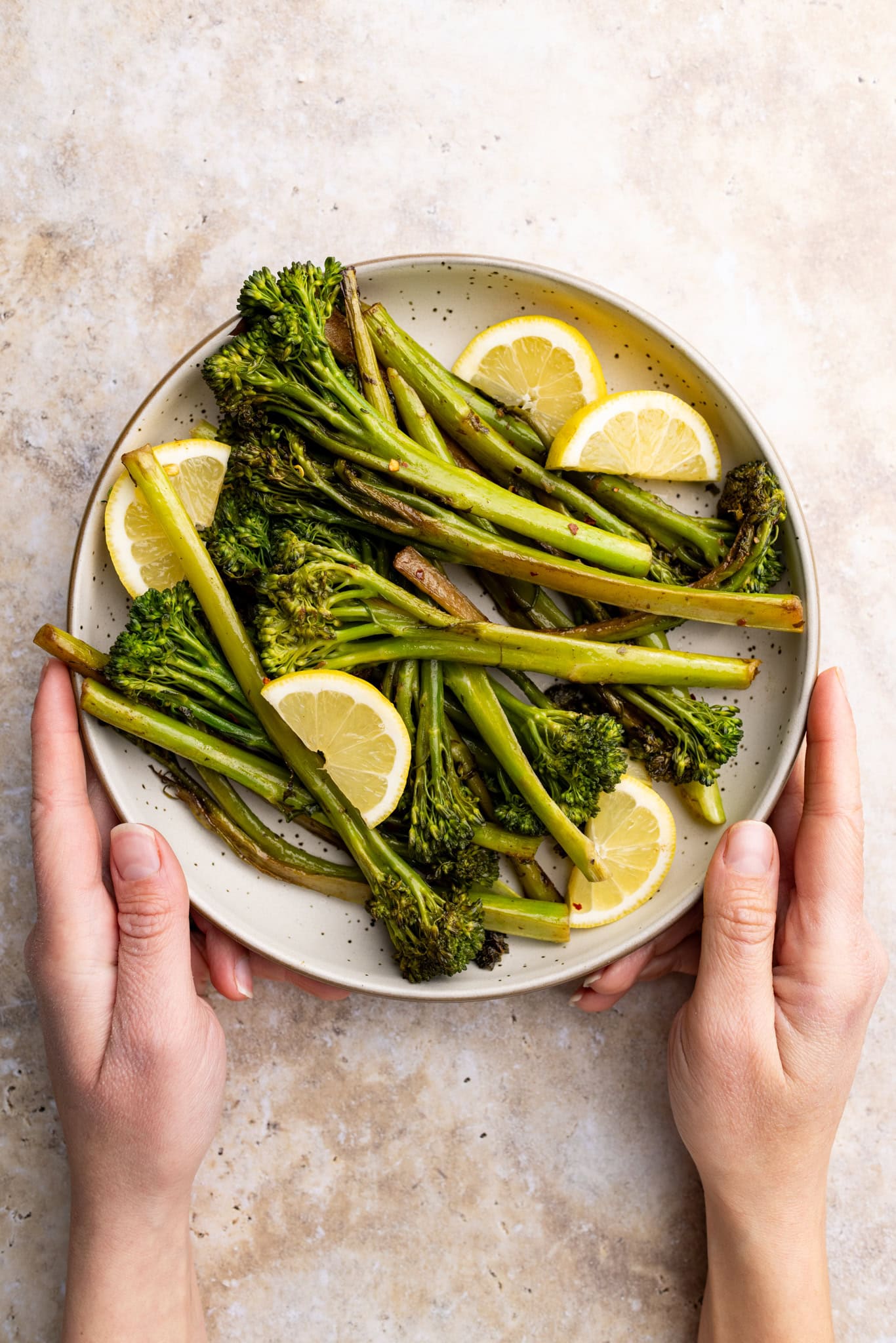 holding a bowl of sautéed broccolini cooked in anchovy butter with lemon wedges.