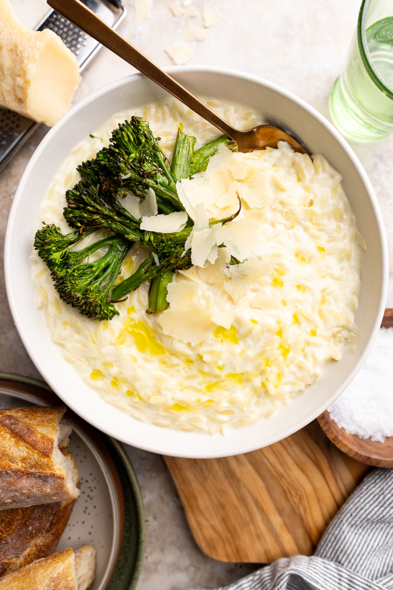 a bowl of parmesan orzo risotto topped with shaved parmesan cheese and roasted broccolini