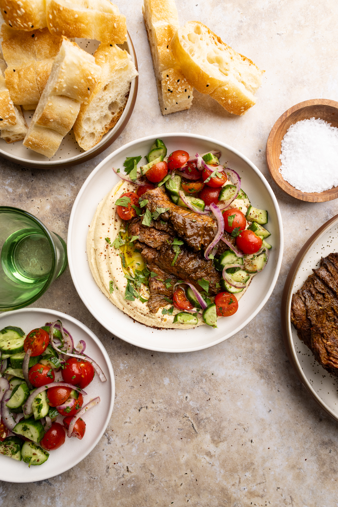bowl of steak shawarma over homemade creamy hummus and topped with a cucumber, tomato, red onion salad.
