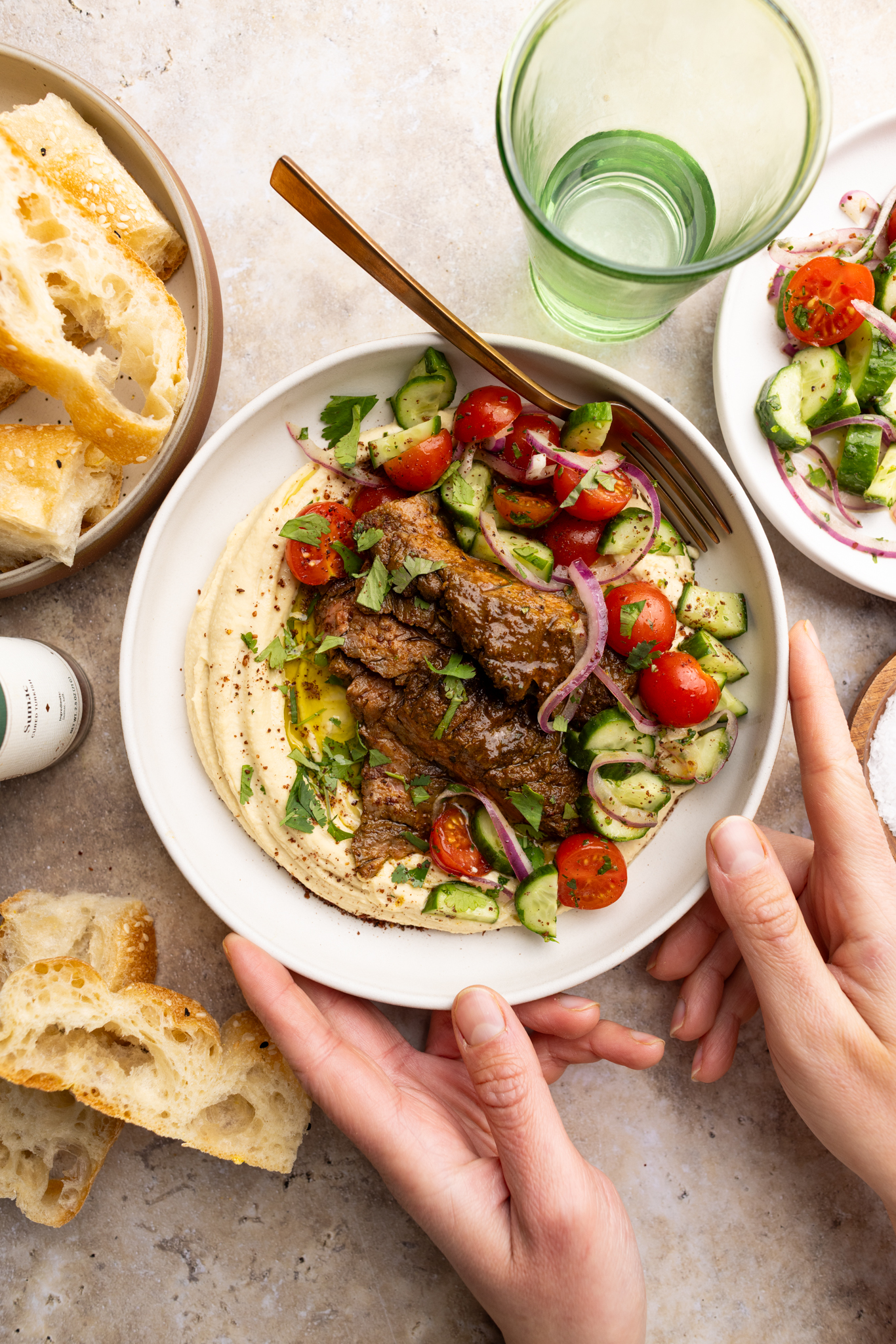 bowl of steak shawarma over homemade creamy hummus and topped with a cucumber, tomato, red onion salad.