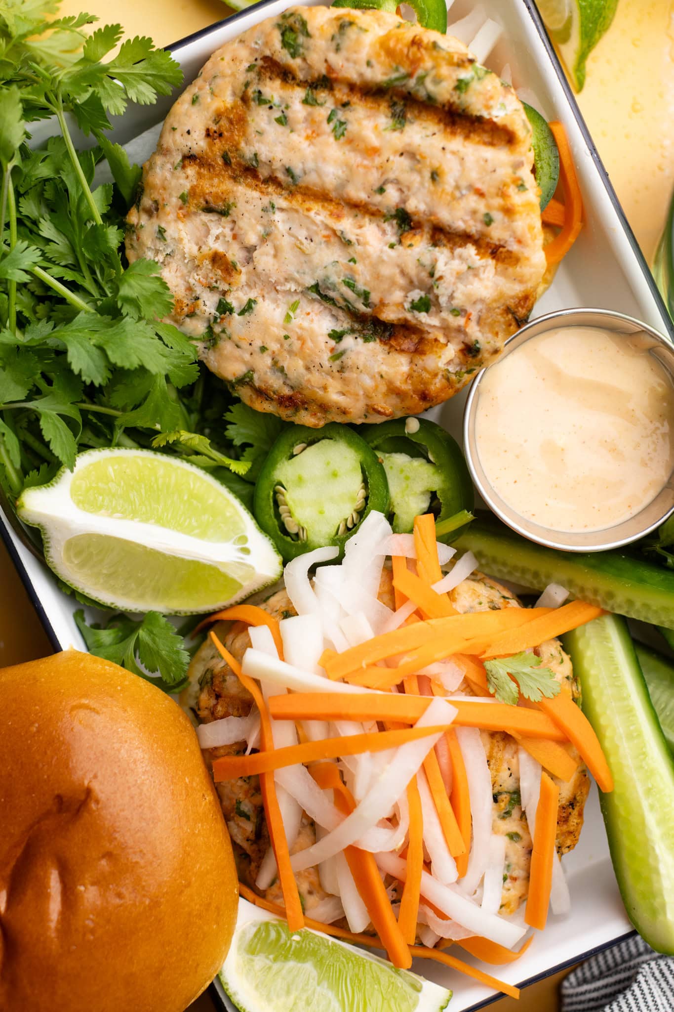 a tray of two banh mi salmon and shrimp burgers topped with pickled diakon and carrots, jalapeños, and cucumber.