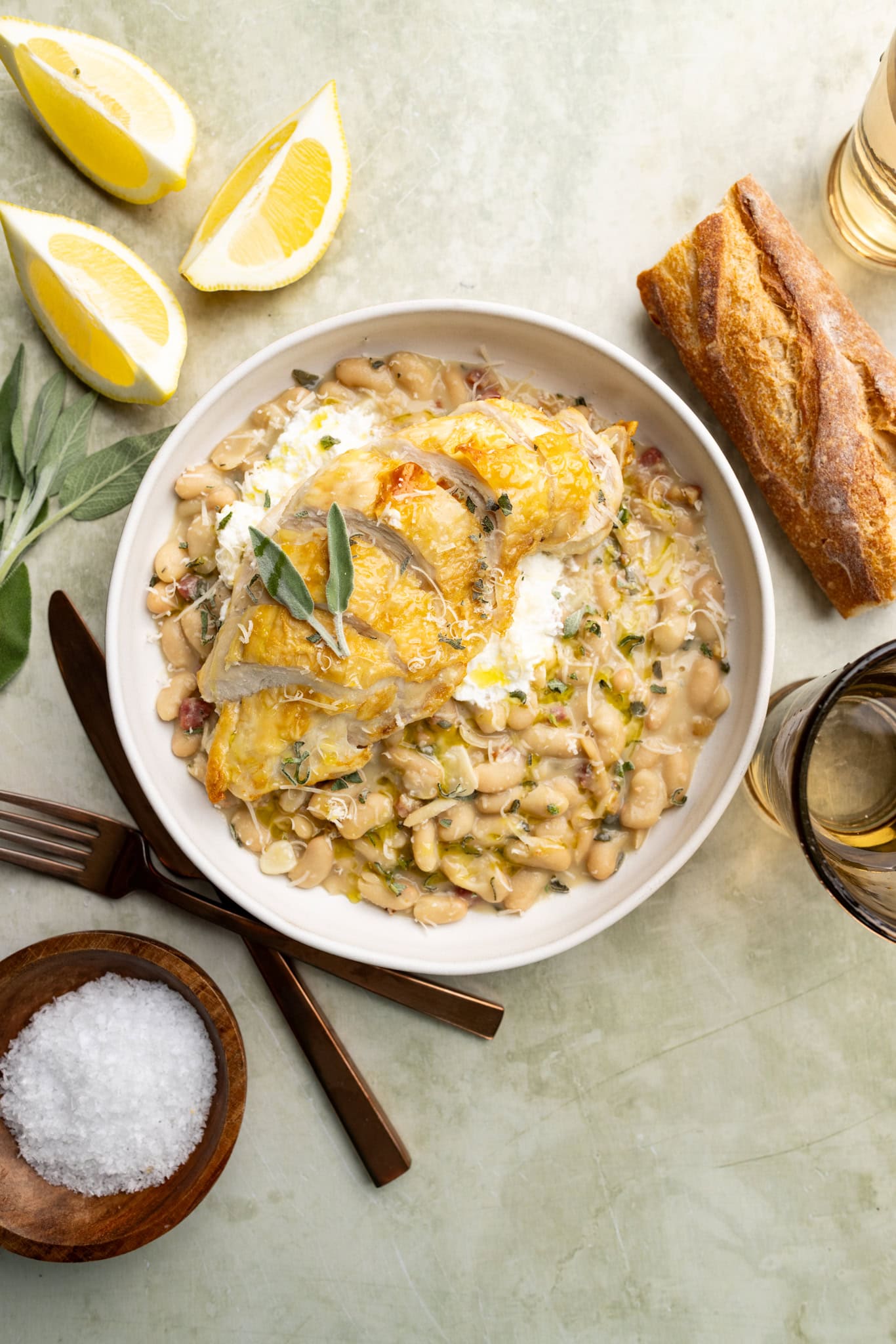 creamy beans with prosciutto and sage in a bowl topped with a crispy chicken skin chicken breast.