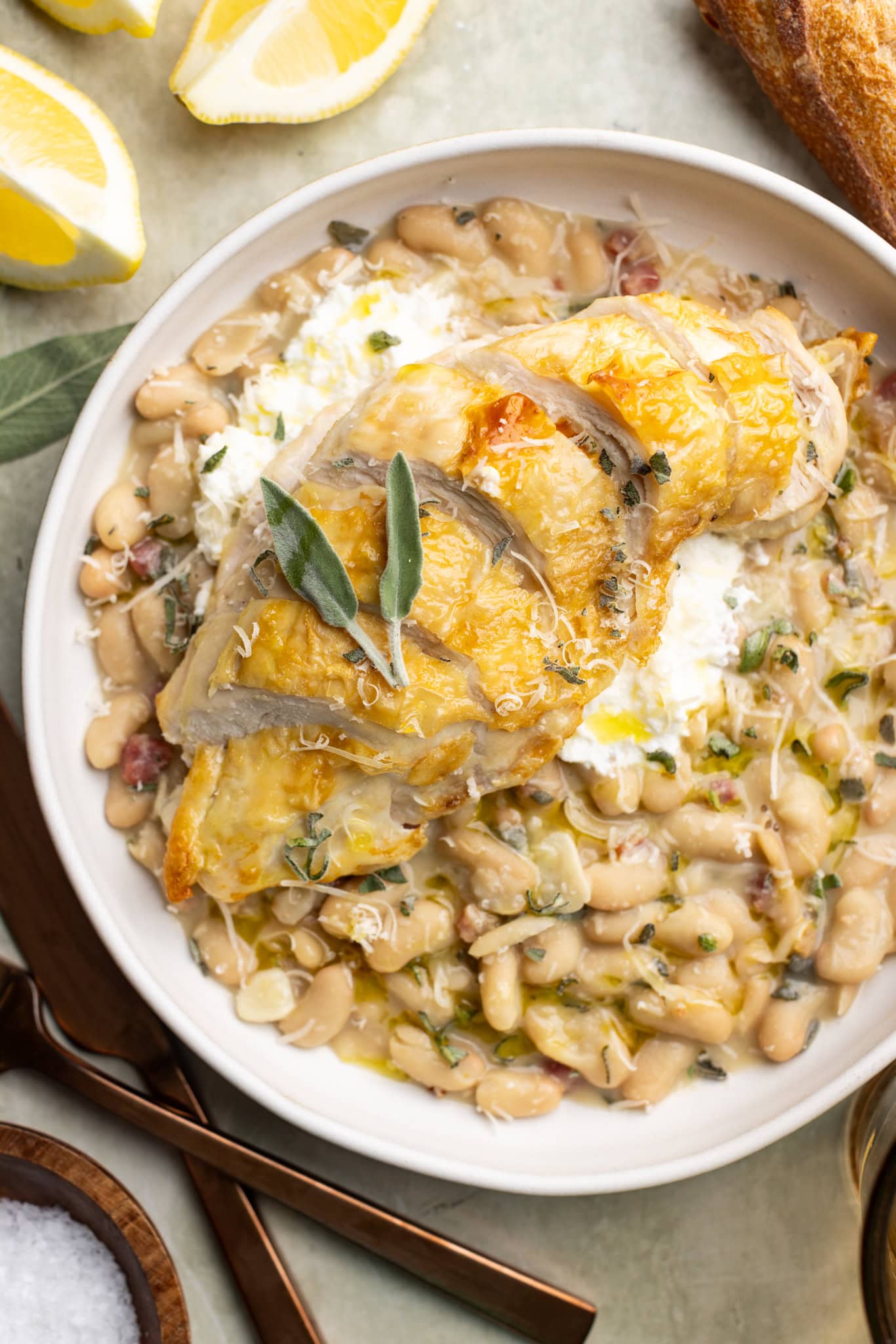 creamy beans with prosciutto and sage in a bowl topped with a crispy chicken skin chicken breast.