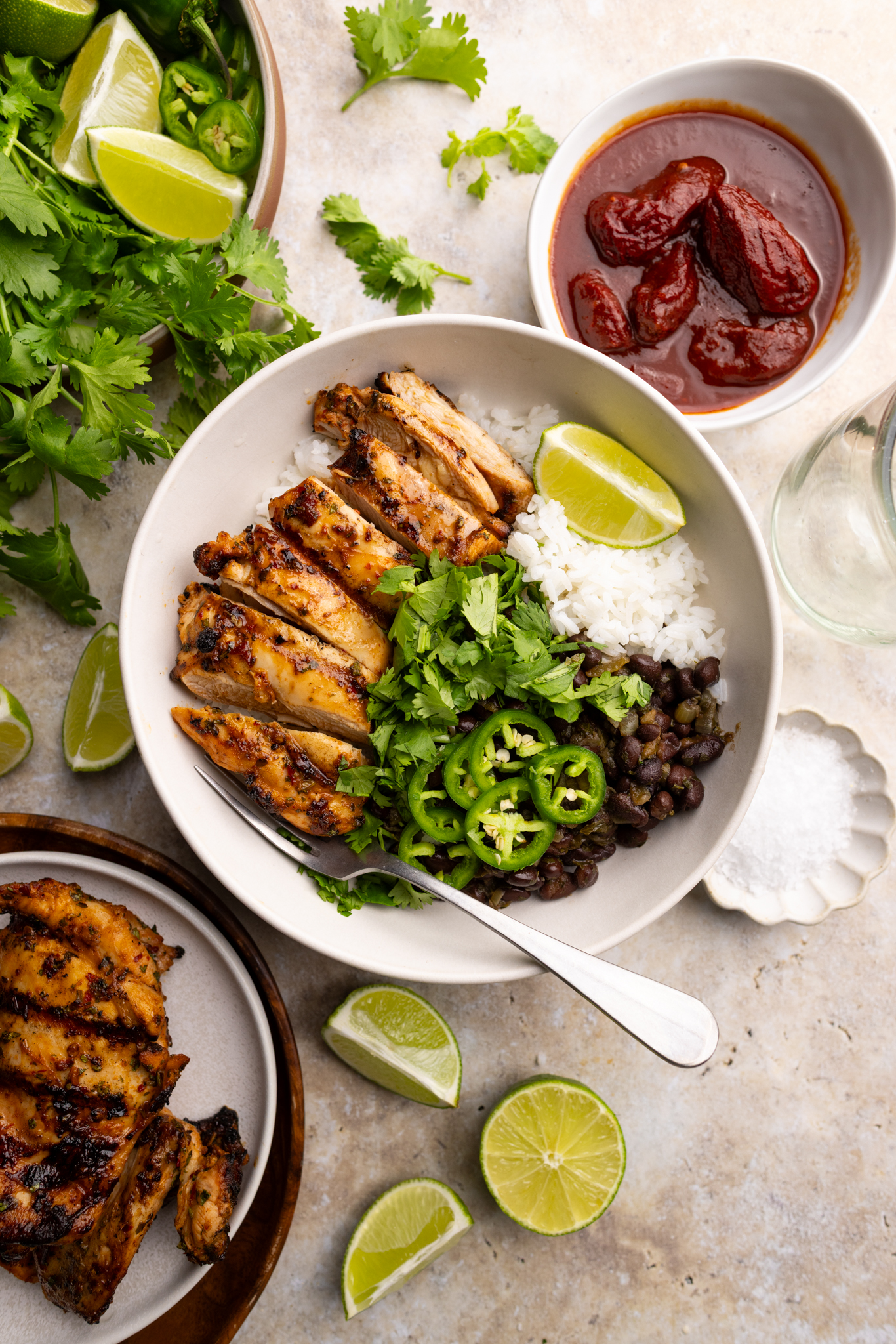 a bowl of grilled chipotle chicken over white rice, black beans, topped with cilantro, jalapeños and a wedge of lime.