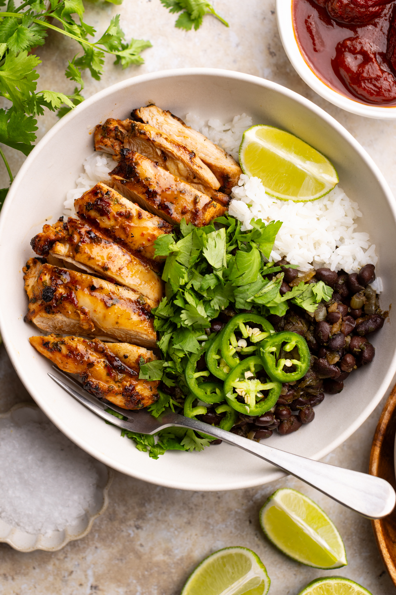 a bowl of grilled chipotle chicken over white rice, black beans, topped with cilantro, jalapeños and a wedge of lime.