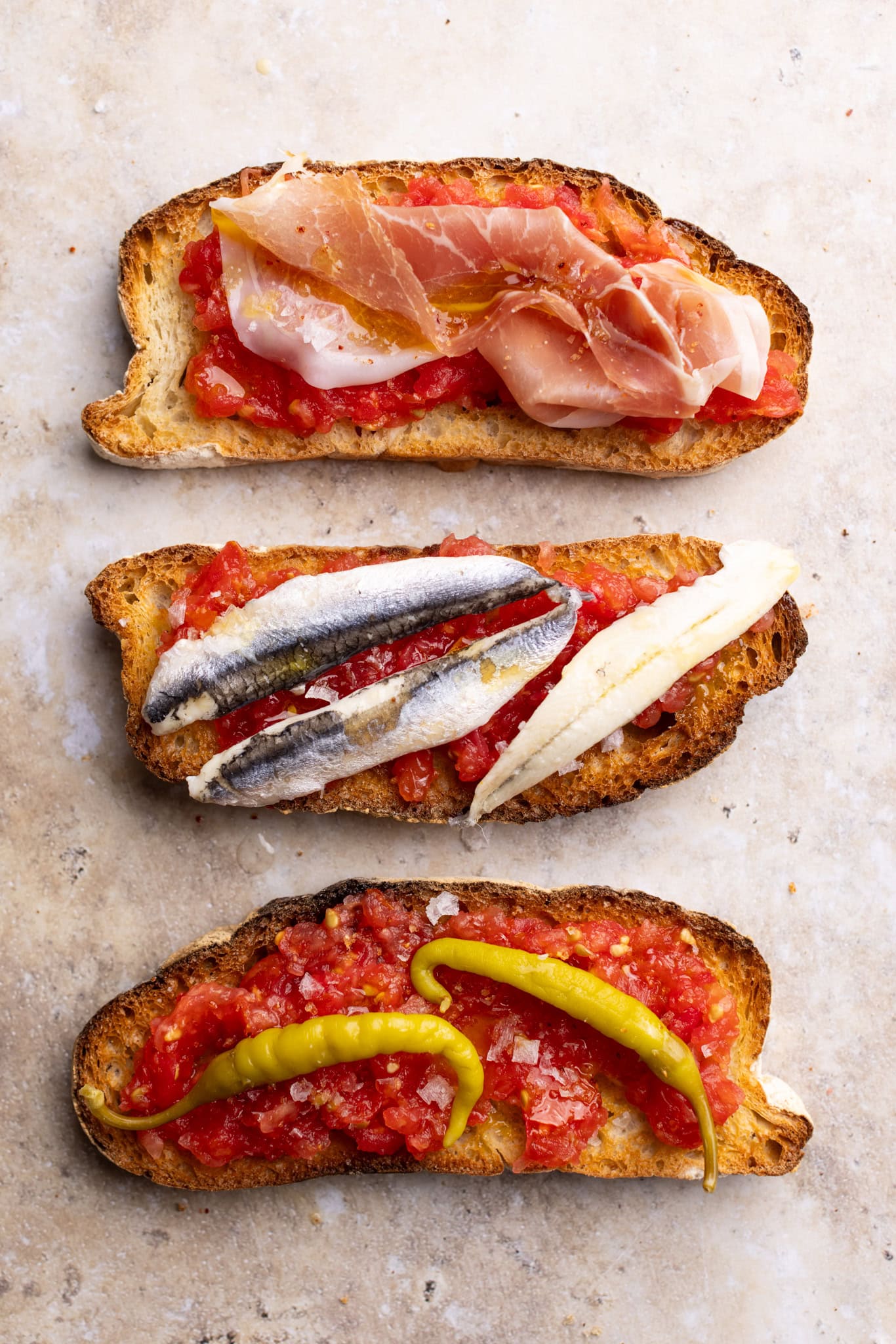3 pan con tomate, topped with anchovies, prosciutto, and peppers