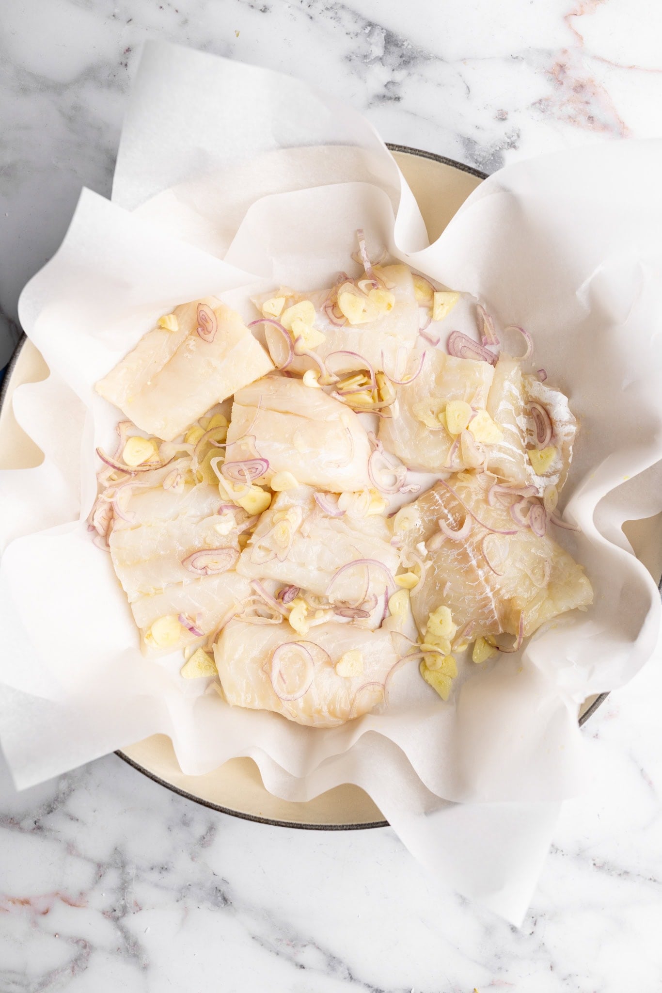 step by step: layering the fish in the braiser with the garlic and onions.