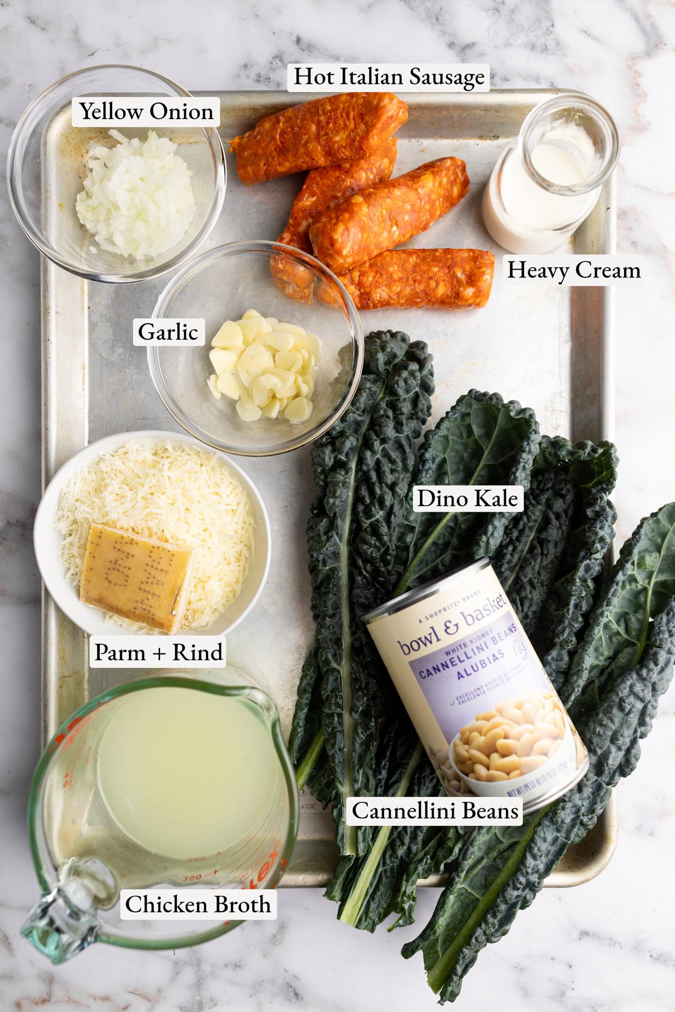 tray of ingredients ( sausage, onion, garlic, heavy cream, dino kale, Parmesan and rind, chicken broth, and white beans.